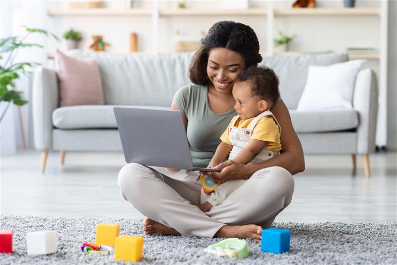 mother and baby sit on floor looking at laptop happily