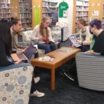 students gather in the QVCC library around a table to study